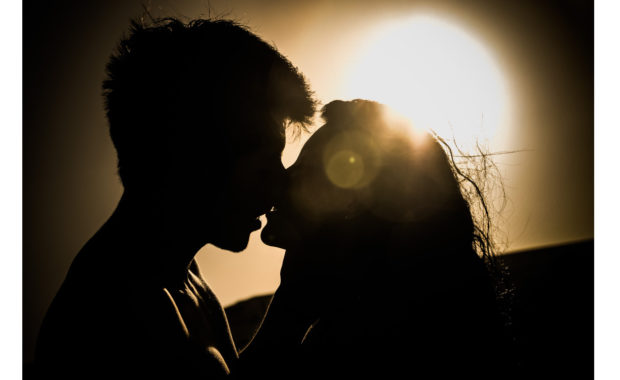 A picture of a couple about to kiss with a sunset in the background