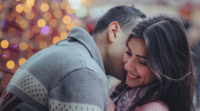 man kissing smiling brunette woman on cheek