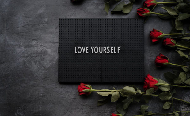 a black sign on a grey table that reads love yourself with red roses around it
