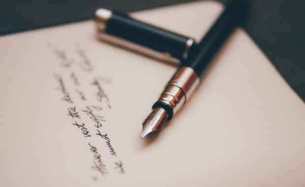 a black pen laying on cursive written words of poetry on a paper