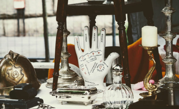 picture of a palmistry hand with the lines of each part of the hand labeled with candlesticks, tins, and jars sitting on the table around it