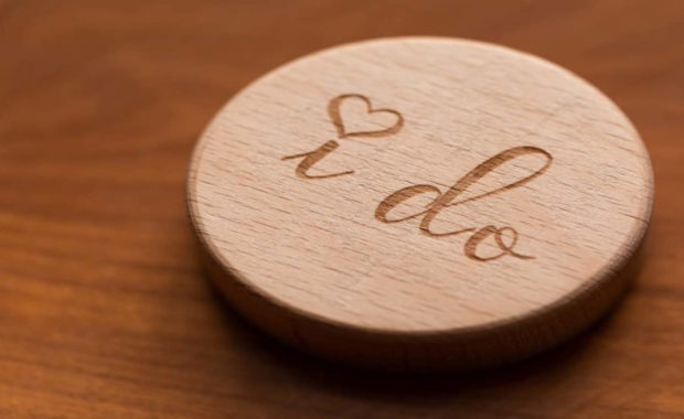 a wooden circle that reads "I do" with a heart dotting the eyes on a table