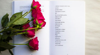 open poetry book on white background with red poems sitting on a page where a love poem is written